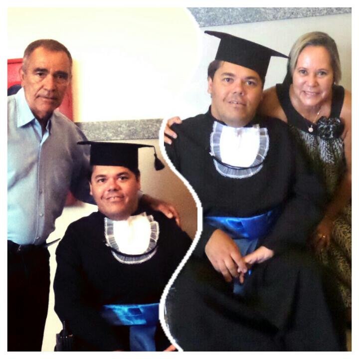 Sidney Reis Borges de beca e capelo no dia da formatura, entre duas pessoas.